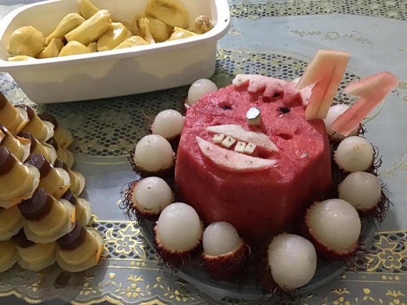 A birthday cake made entirely of various fruits, with a quirky human face design.