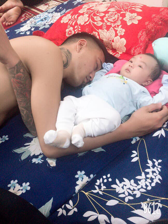The baby stares at the ceiling while her dad is sleeping soundly beside her.
