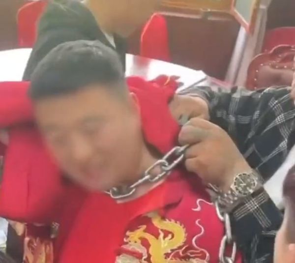 Image of the groom struggling with a heavy chain around his neck on his wedding day